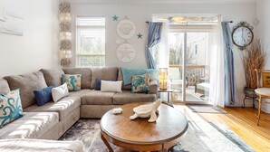 A cozy living room with a sectional sofa, a round coffee table, and a view of the outside through a glass door.