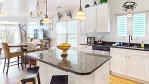 A spacious kitchen with white cabinetry, a granite countertop island, and pendant lighting.