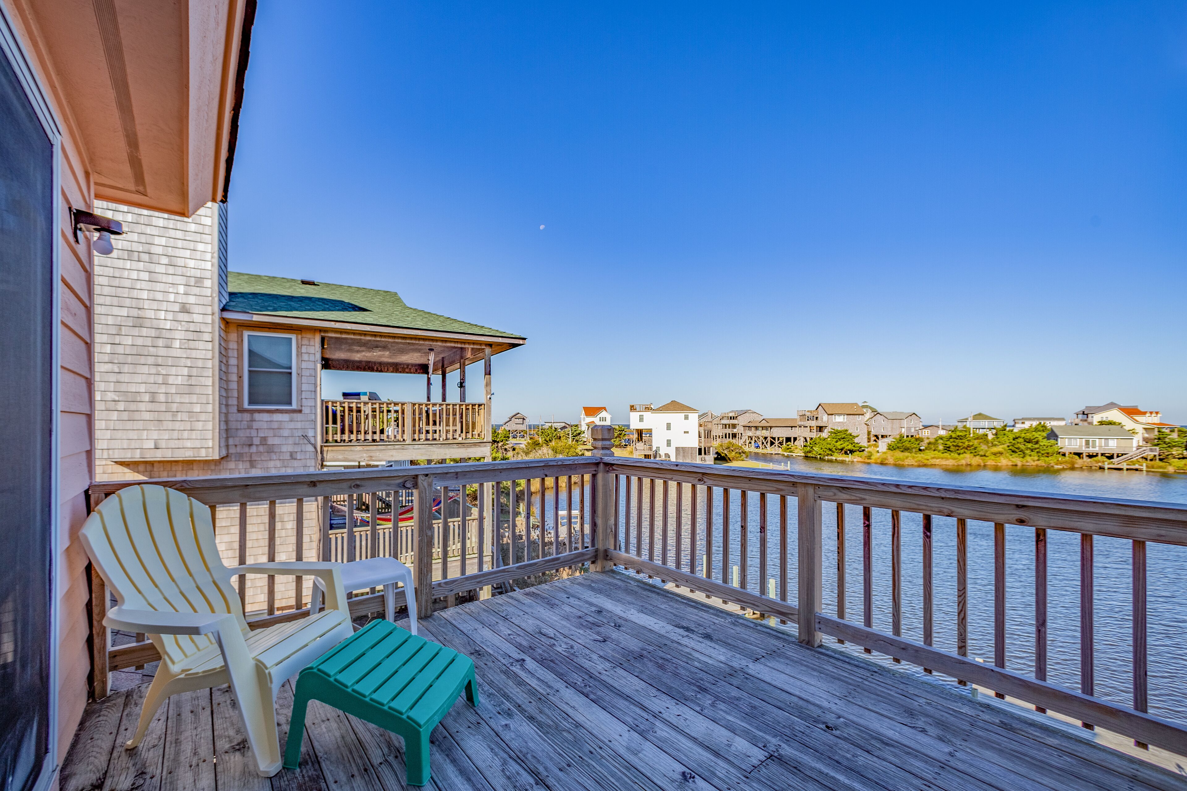 A wooden deck with two chairs and a table, overlooking a body of water and houses.