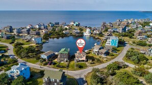 An aerial view of a coastal residential area with houses, a dock, and a body of water. - Sea Dream 440: Lagoon-front home w/private dock (Avon)