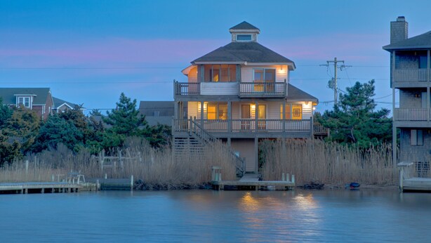 A two-story waterfront house with a balcony, dock, and surrounding vegetation. - Sea Dream 440: Lagoon-front home w/private dock (Avon)