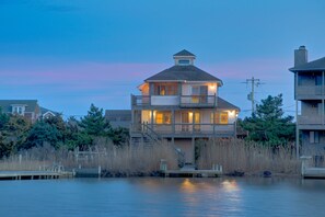 Ein zweistöckiges Haus am Wasser mit Balkon, Anlegesteg und umgebender Bepflanzung.