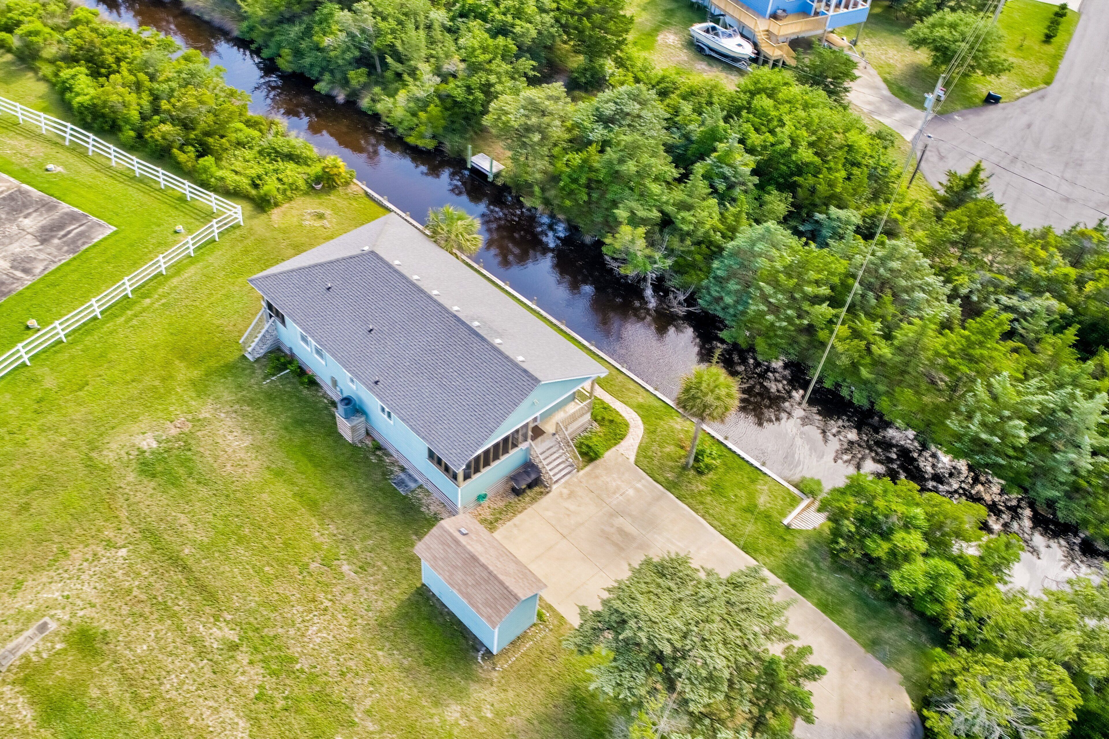 An aerial view of a house with a large garage, a fenced yard, and a river nearby.