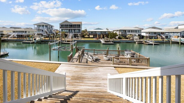 A marina with docked boats, a wooden deck, and a view of several houses with balconies. - Canal front home with a floating dock and large deck with sound views (Topsail Beach)