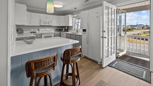 A modern kitchen with white cabinets, a large island, and two wicker bar stools. - Canal front home with a floating dock and large deck with sound views (Topsail Beach)