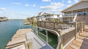 A waterfront property with multiple buildings, a dock, and a wooden walkway. - Canal front home with a floating dock and large deck with sound views (Topsail Beach)