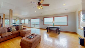 A spacious living room with a large sectional sofa, a wooden coffee table, and a ceiling fan. - Waterfront home with pool, private hot tub, ocean view, W/D & AC - dog-friendly (Frisco)