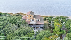 A two-story house with a large balcony, surrounded by dense greenery and a view of the sea. - Waterfront home with pool, private hot tub, ocean view, W/D & AC - dog-friendly (Frisco)