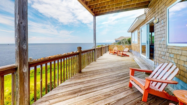 A wooden deck with a railing, wooden chairs, and a view of the ocean. - Waterfront home with pool, private hot tub, ocean view, W/D & AC - dog-friendly (Frisco)
