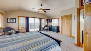 A bedroom with a large bed, a ceiling fan, a dresser, and a view of the outdoors. - Waterfront home with pool, private hot tub, ocean view, W/D & AC - dog-friendly (Frisco)