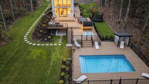 A modern house with a large deck, a swimming pool, and a well-maintained lawn.