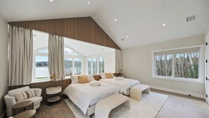 A spacious bedroom with two large beds, a sofa, a small round table, and a large window providing a view of trees.