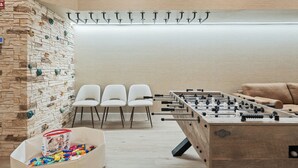 Una habitación con mesa de futbolín, sofá y pared equipada con presas de escalada.