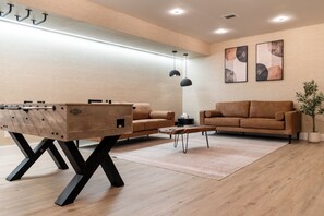 A modern living room with a wooden coffee table, two sofas, and a foosball table. - Lakefront Paradise w/Pool, Hot Tub, Sauna & Kayaks (Woodridge)