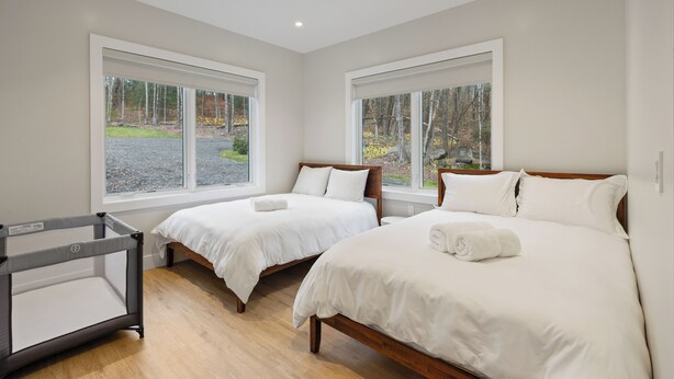 Un dormitorio con dos camas individuales, una cuna y ventanas amplias con vistas a árboles.