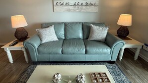 A teal leather sofa with two lamps, a coffee table with decorative items, and a wall-mounted artwork. - Lovely beachfront condo with beach access, central AC, washer/dryer & fast WiFi (Carolina Beach)