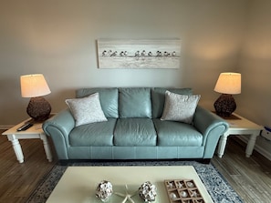 A teal leather sofa with two lamps, a coffee table with decorative items, and a wall-mounted artwork.