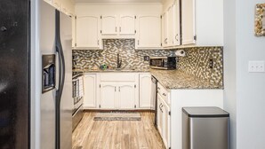 A kitchen with white cabinets, a stainless steel refrigerator, a microwave, and a trash can. - Lovely beachfront condo with beach access, central AC, washer/dryer & fast WiFi (Carolina Beach)