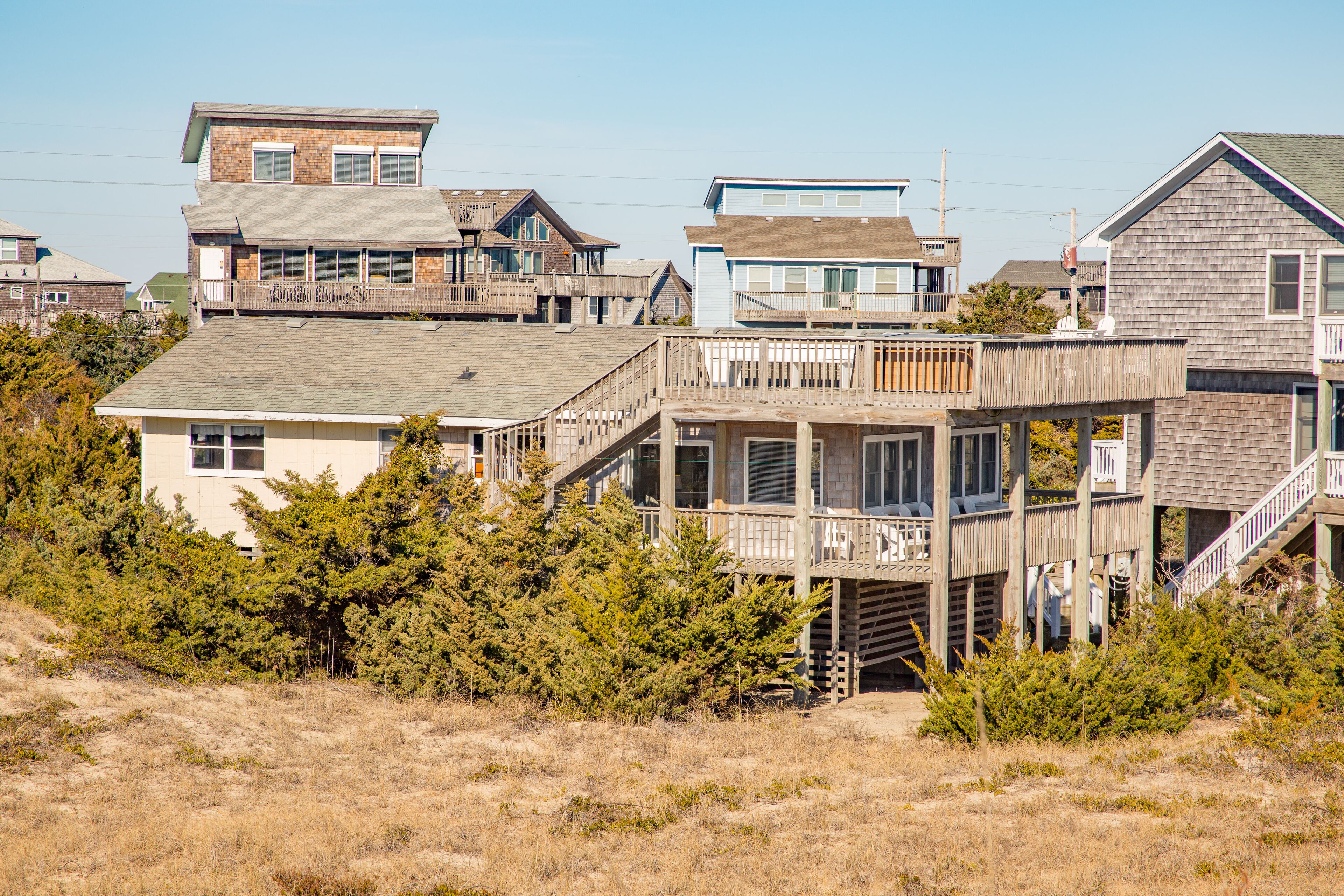 A coastal residential area with multiple houses, including a prominent wooden structure with a balcony and a staircase leading to a second floor.