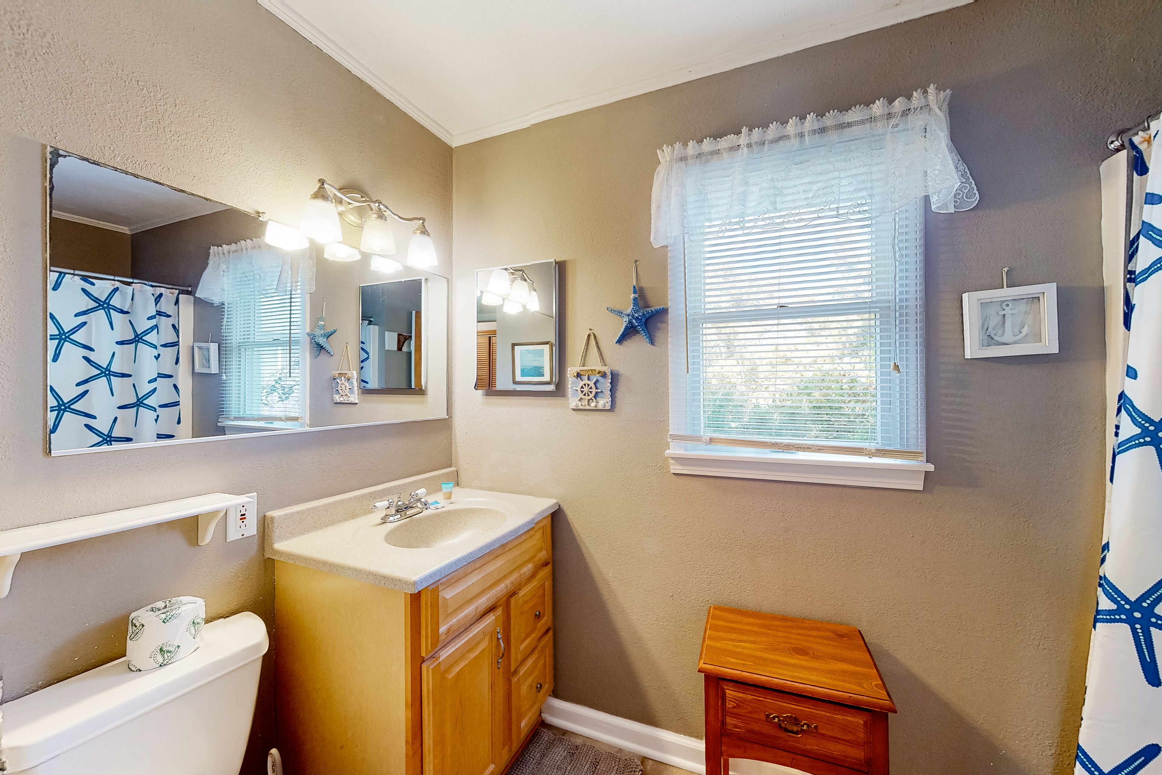 A bathroom with a sink, vanity, mirror, and window.