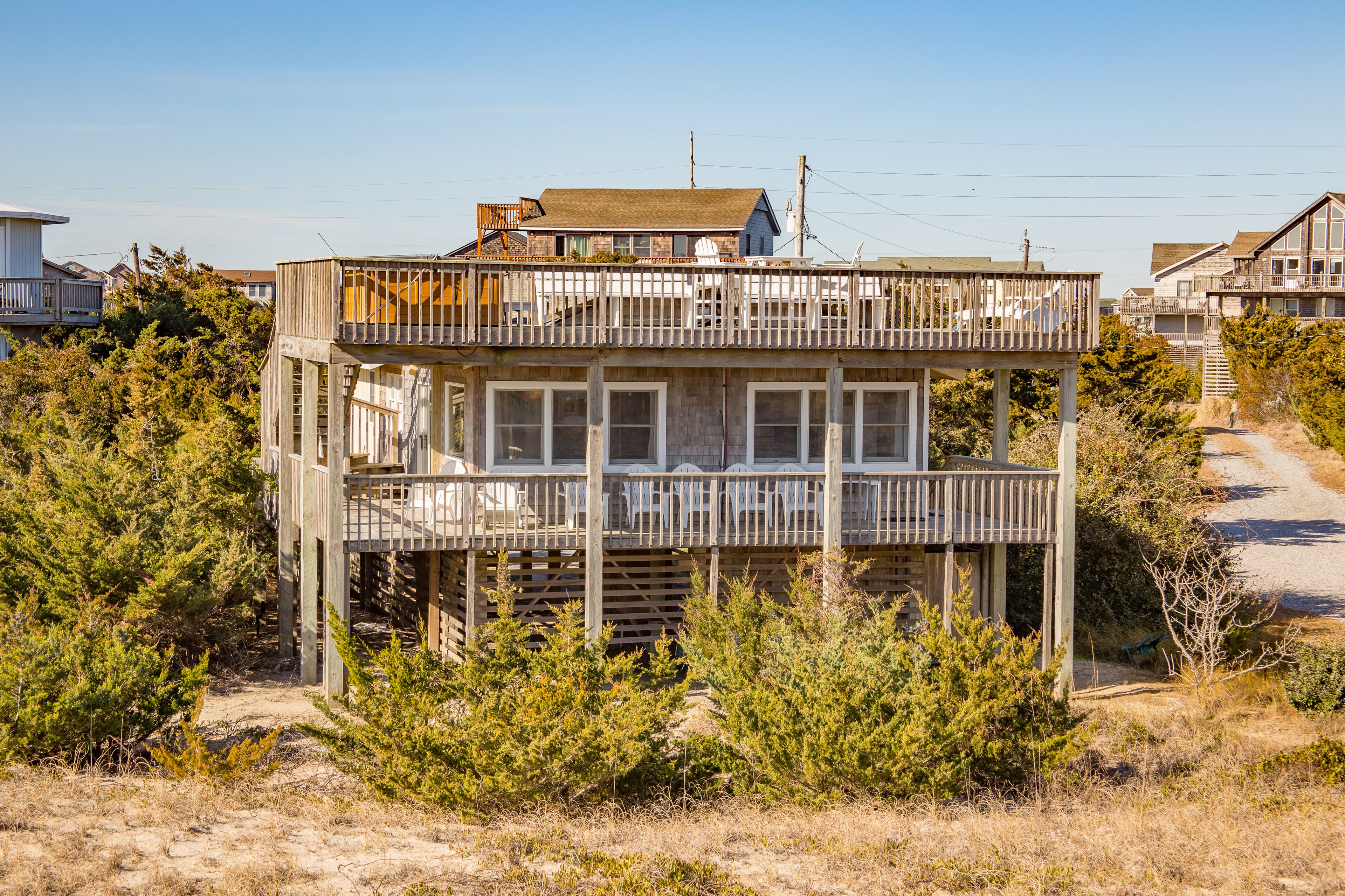A two-story wooden house with a balcony, surrounded by dry grass and pine trees.
