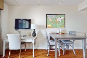 Ein Zimmer mit Holzboden, einem weißen Schreibtisch, einem Fernseher, einer Lampe und einer Karte an der Wand.