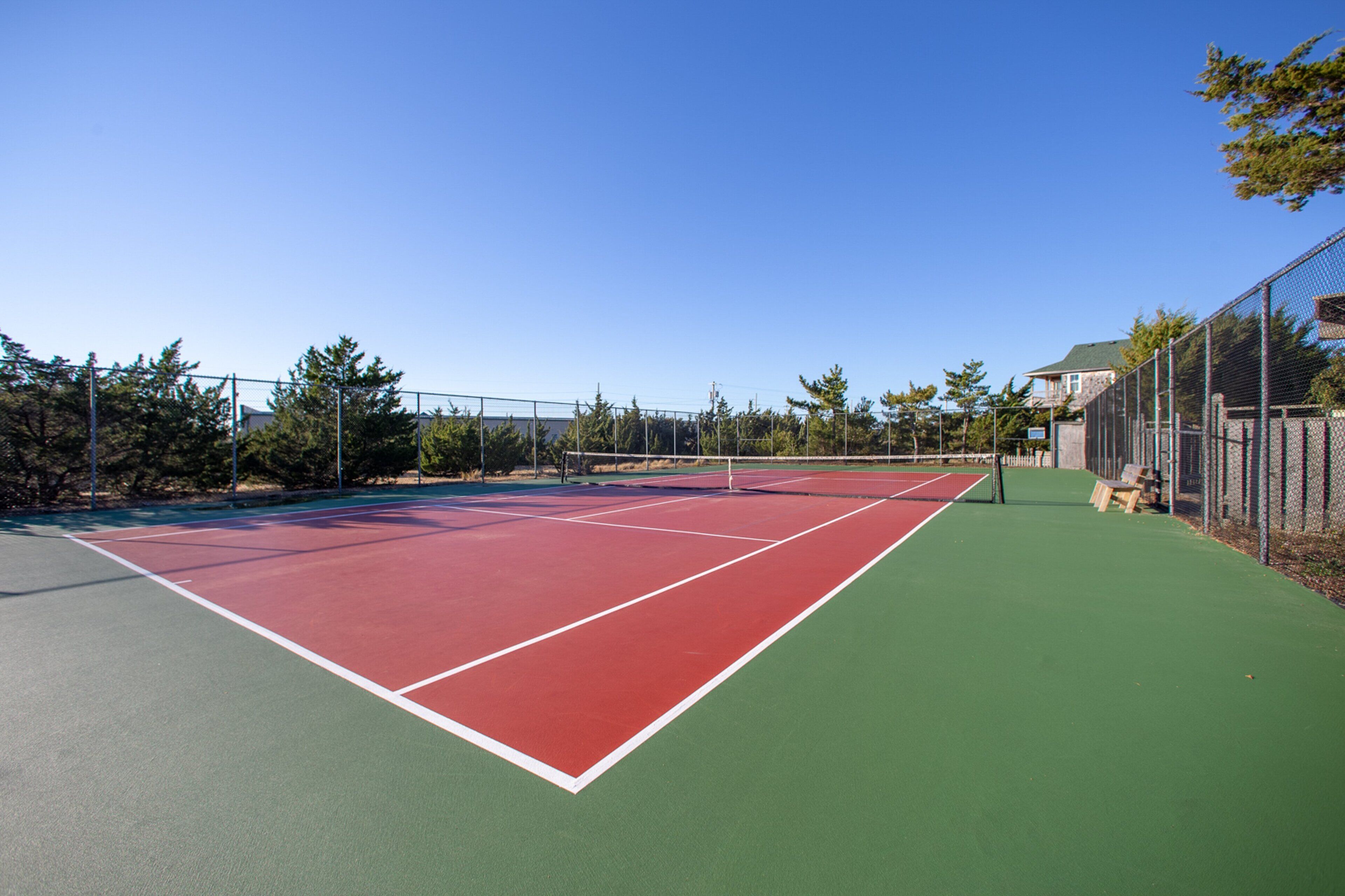 Ein Tennisplatz im Freien mit roter und grüner Belag, umgeben von einem Maschendrahtzaun und Bäumen.