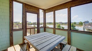 Eine Holzterrasse mit Tisch und Bänken, mit Blick auf einen See und Gebäude im Hintergrund.