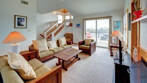 Ein geräumiges Wohnzimmer mit einer Holztreppe, gemütlicher Sitzgelegenheiten und einem großen Schiebeglastür, die zu einem Außenbereich führt.