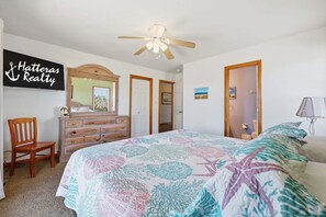 A bedroom with a bed, a dresser, a chair, a ceiling fan, and a sign on the wall.