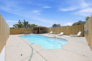A backyard with a swimming pool, wooden fence, and a covered seating area.
