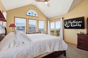 A bedroom with a bed, a ceiling fan, a large window, and a view of the ocean.