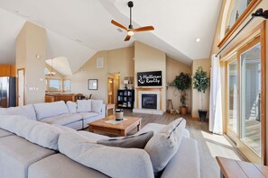 A spacious living room with a large sofa, a fireplace, and a ceiling fan.