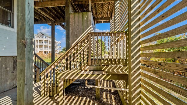 A wooden staircase with a metal handrail leading to a covered outdoor area. - Ocean-view home with pool, hot tub, grill, decks & pool table (Waves)