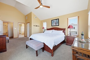 A bedroom with a large bed, a wooden bench, a desk, and a ceiling fan. - Ocean-view home with pool, hot tub, grill, decks & pool table (Waves)