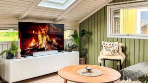 Ein gemütliches Wohnzimmer mit Fernseher, der einen Kamin zeigt, einem runden Holztisch und bequemen Sitzgelegenheiten.