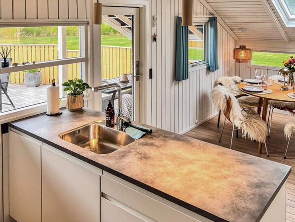 A kitchen with a large window, a sink, and a dining area with a table and chairs. - 6 Person Holiday Home in Vaeggerlose (Vaeggerlose)