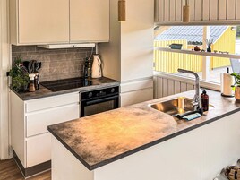 Et moderne køkken med en stor ø, indbygget ovn og et vindue med udsigt til en gul bygning.