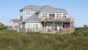 A two-story house with a balcony and a deck, surrounded by vegetation. - Oceanfront dog-friendly home close to sand with views & private hot tub (Buxton)