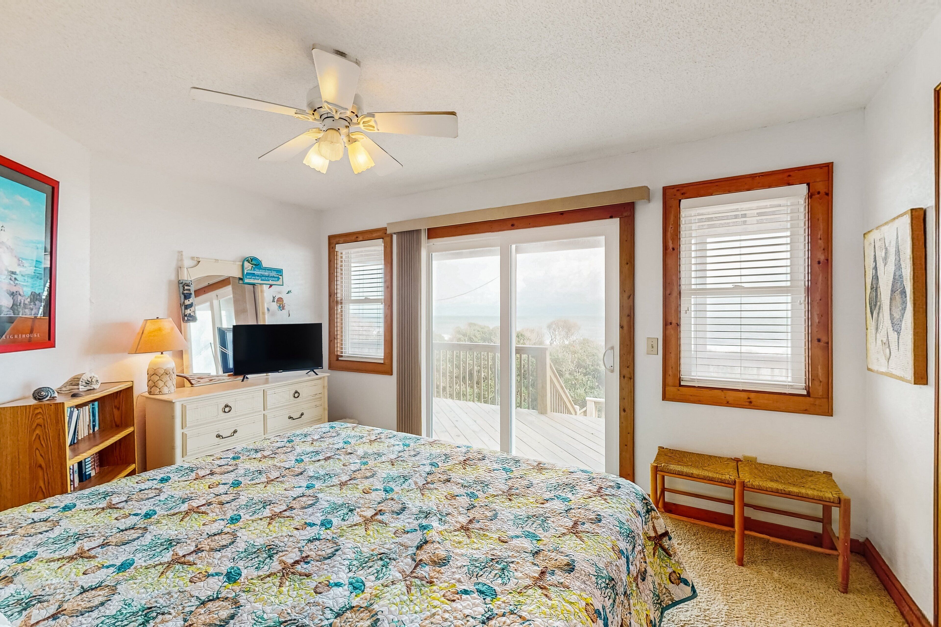 A bedroom with a large bed, a ceiling fan, a TV, a dresser, and a bench.