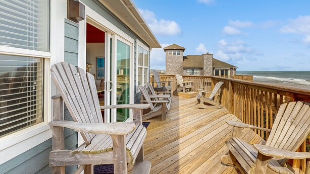 A wooden deck with Adirondack chairs, a glass door leading to a room, and a view of the ocean. - Oceanfront dog-friendly home close to sand with views & private hot tub (Buxton)