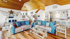 A spacious living area with a wooden ceiling, a large star decoration, and a kitchen in the background. - Oceanfront dog-friendly home close to sand with views & private hot tub (Buxton)