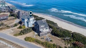 An aerial view of a coastal residential area with houses near the beach, a marked location, and a road. - Oceanfront dog-friendly home close to sand with views & private hot tub (Buxton)