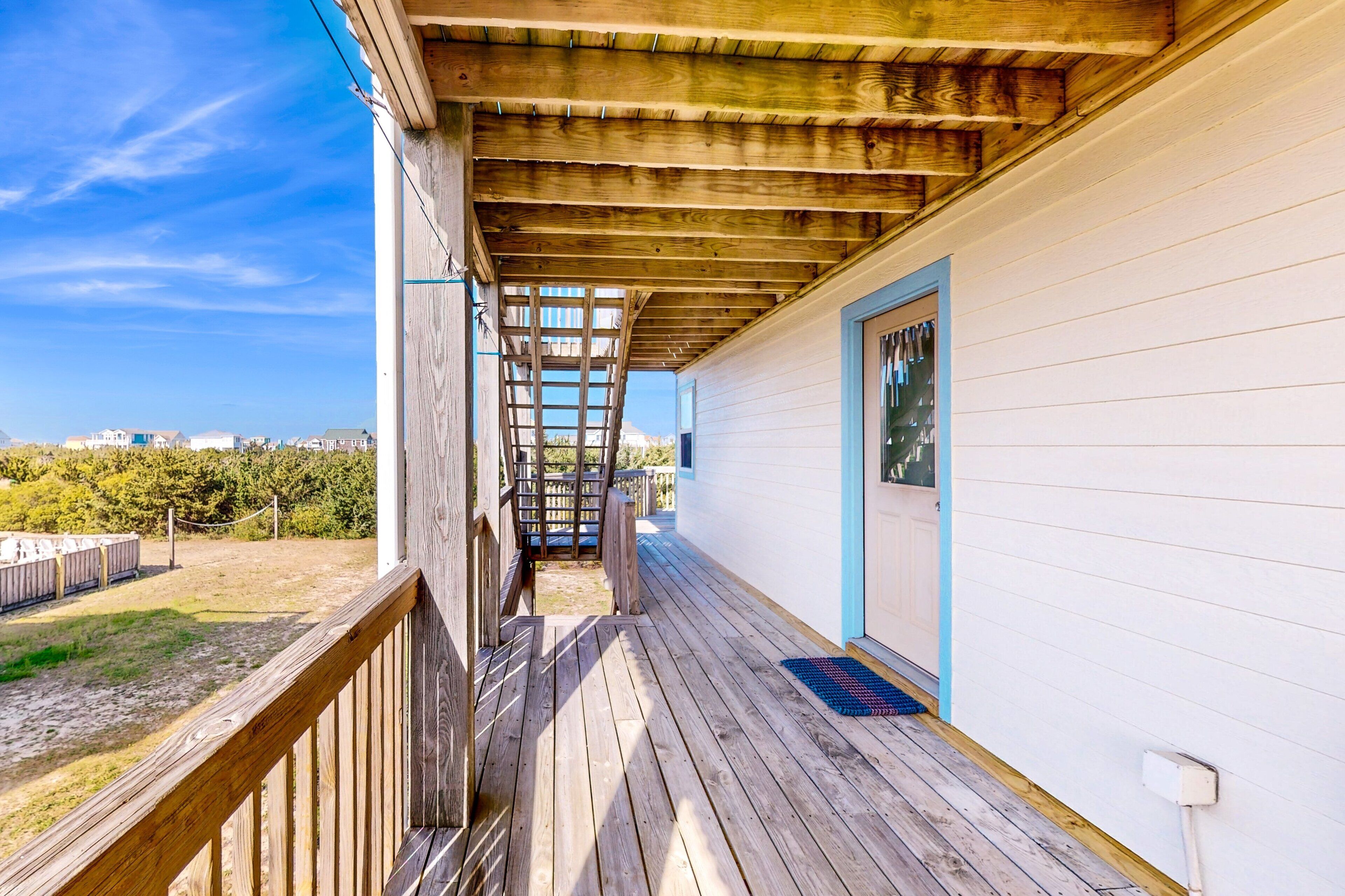 A wooden deck leading to a white building with a blue door, a wooden staircase, and a view of the surrounding area.