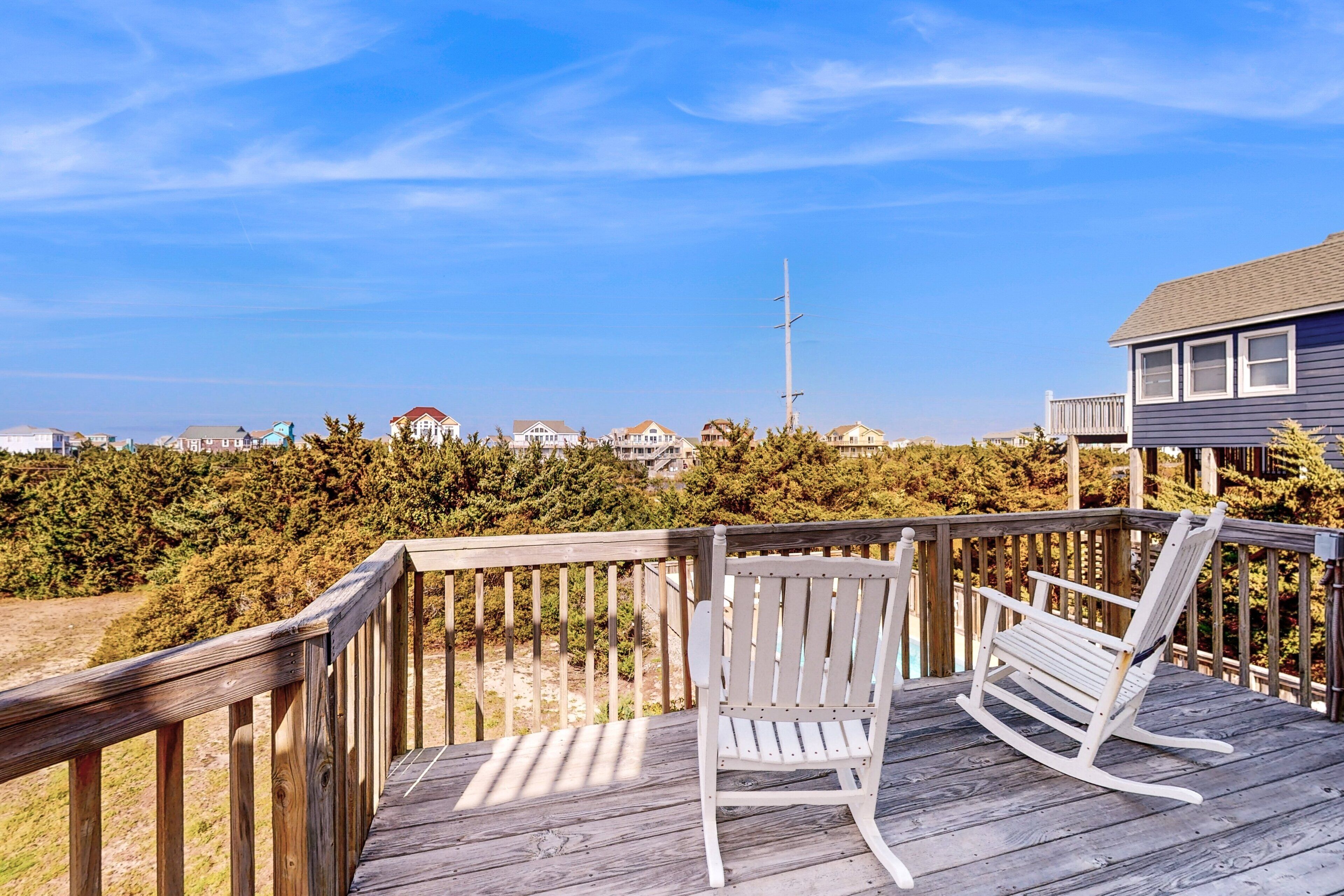 A wooden deck with two rocking chairs overlooking a residential area and a clear sky.
