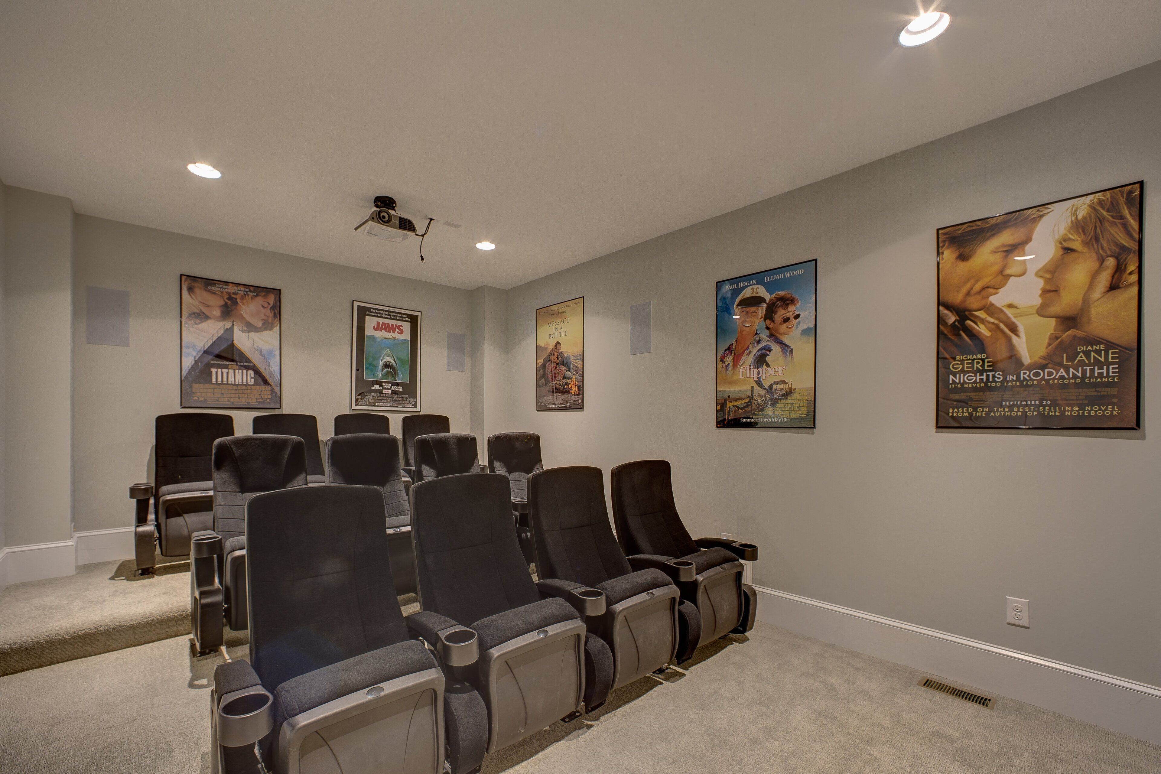 Une salle de cinéma privée dotée de plusieurs rangées de fauteuils de cinéma noirs, d’un sol recouvert de moquette et d’un projecteur au plafond.