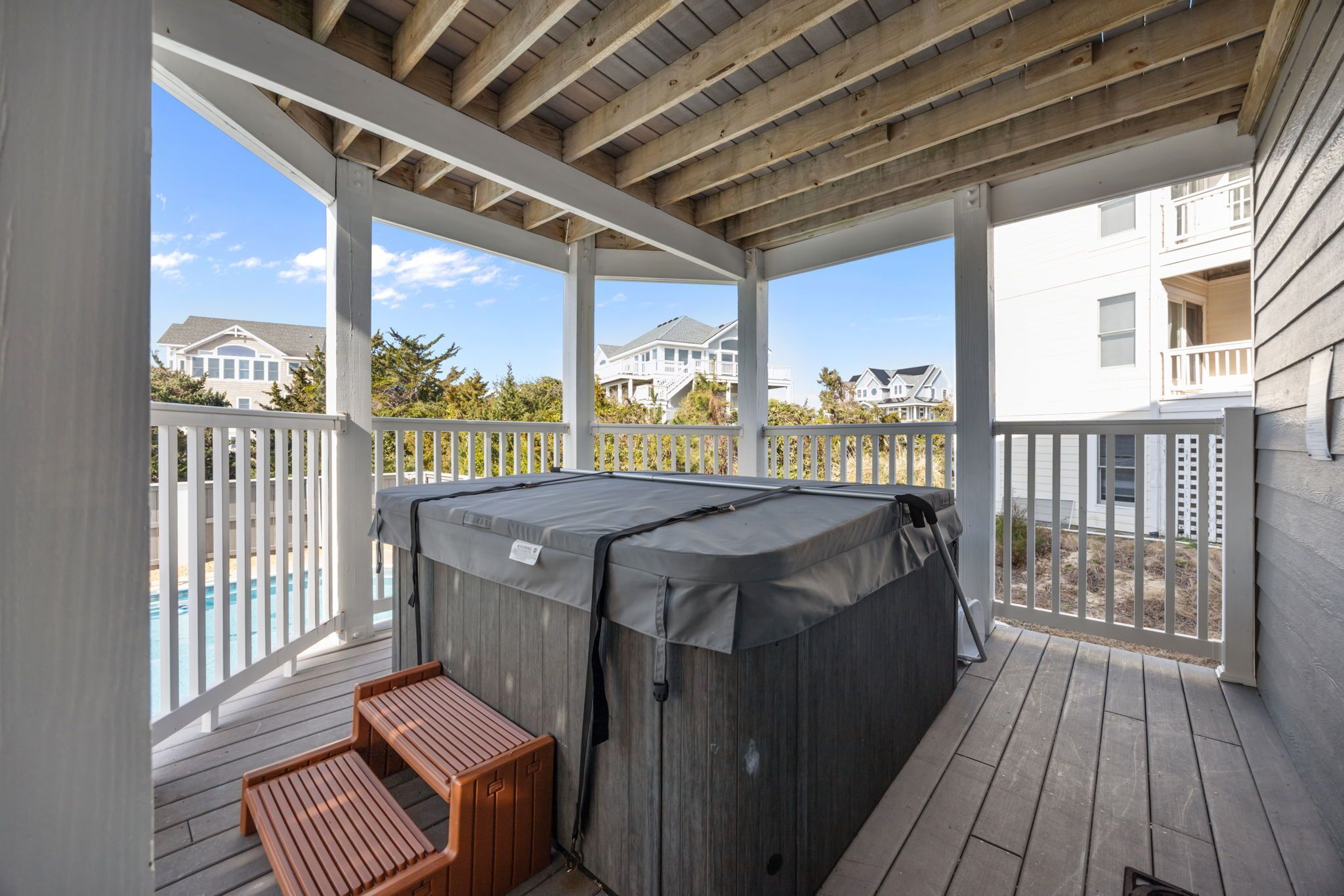 Un espace extérieur abrité comprenant un jacuzzi, une terrasse en bois et des garde-corps blancs.