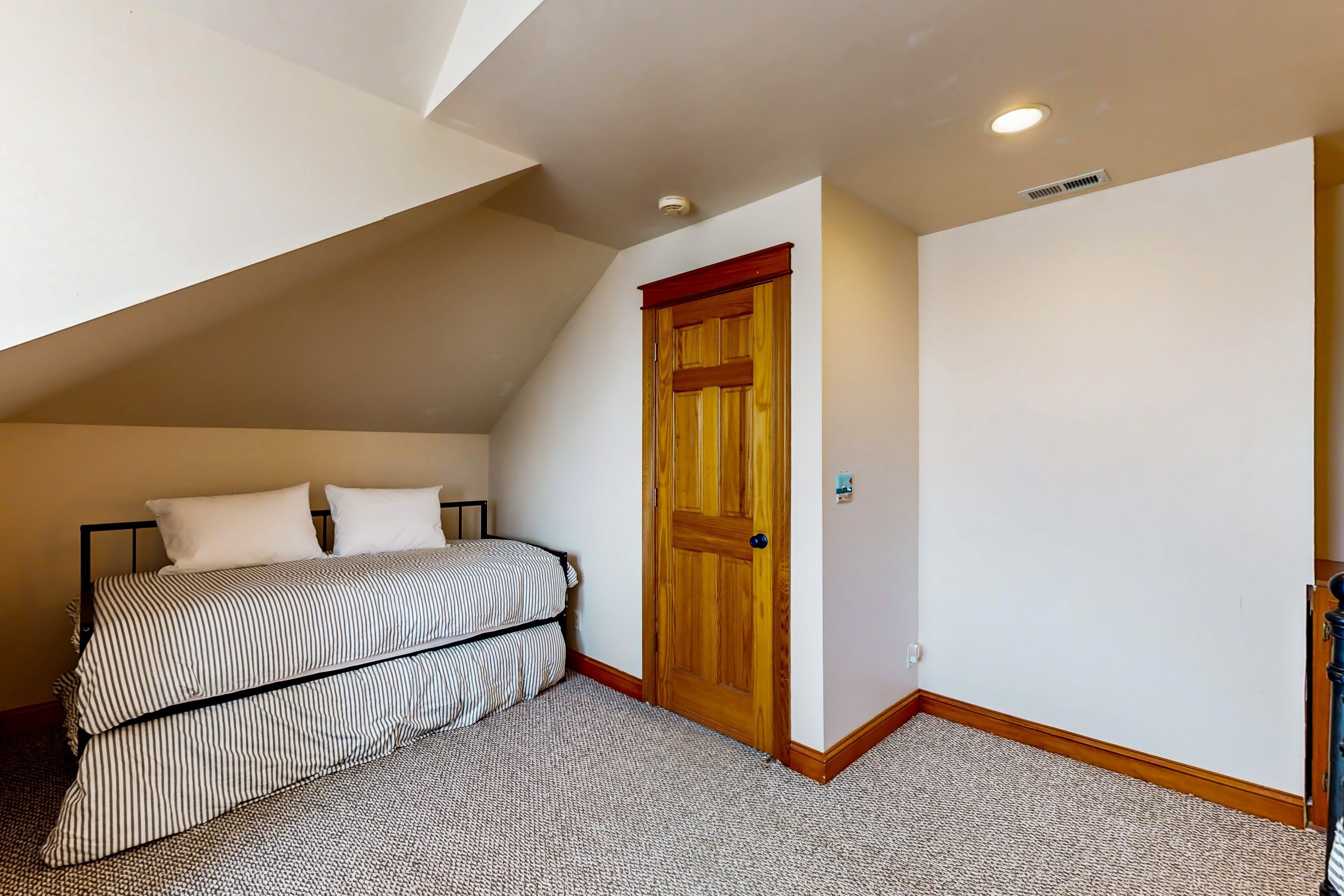 Un dormitorio con techo inclinado, una puerta de madera y una cama con ropa de cama a rayas.