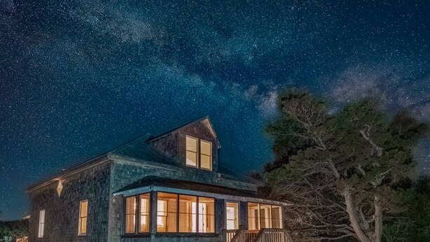 Une maison de campagne rustique avec un porche, sous un ciel étoilé.