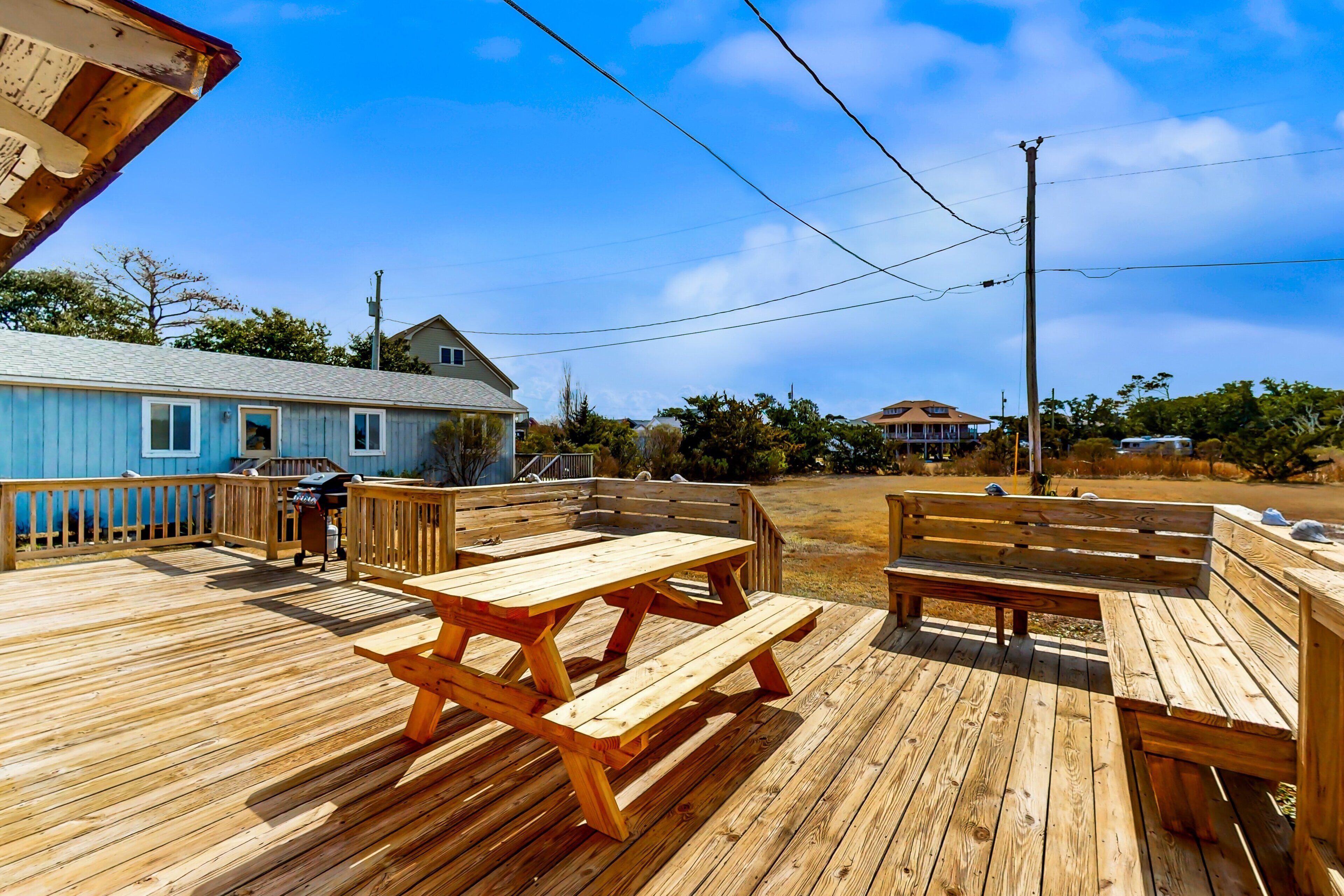 A wooden deck with picnic tables and a barbecue grill.